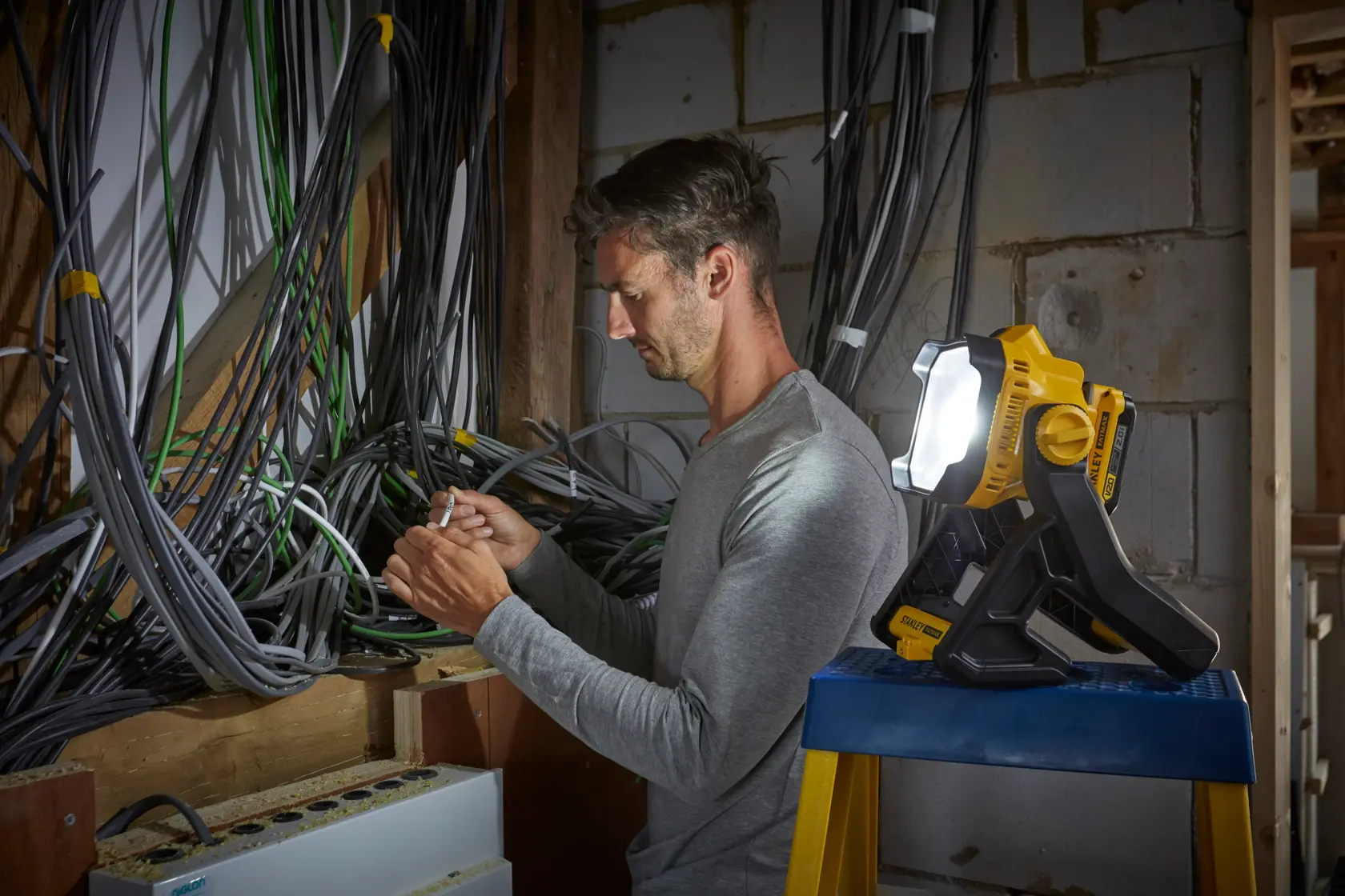 Stanley SFMCL030B luz de trabajo iluminando electricista trabajando entre cables en pared sin terminar.