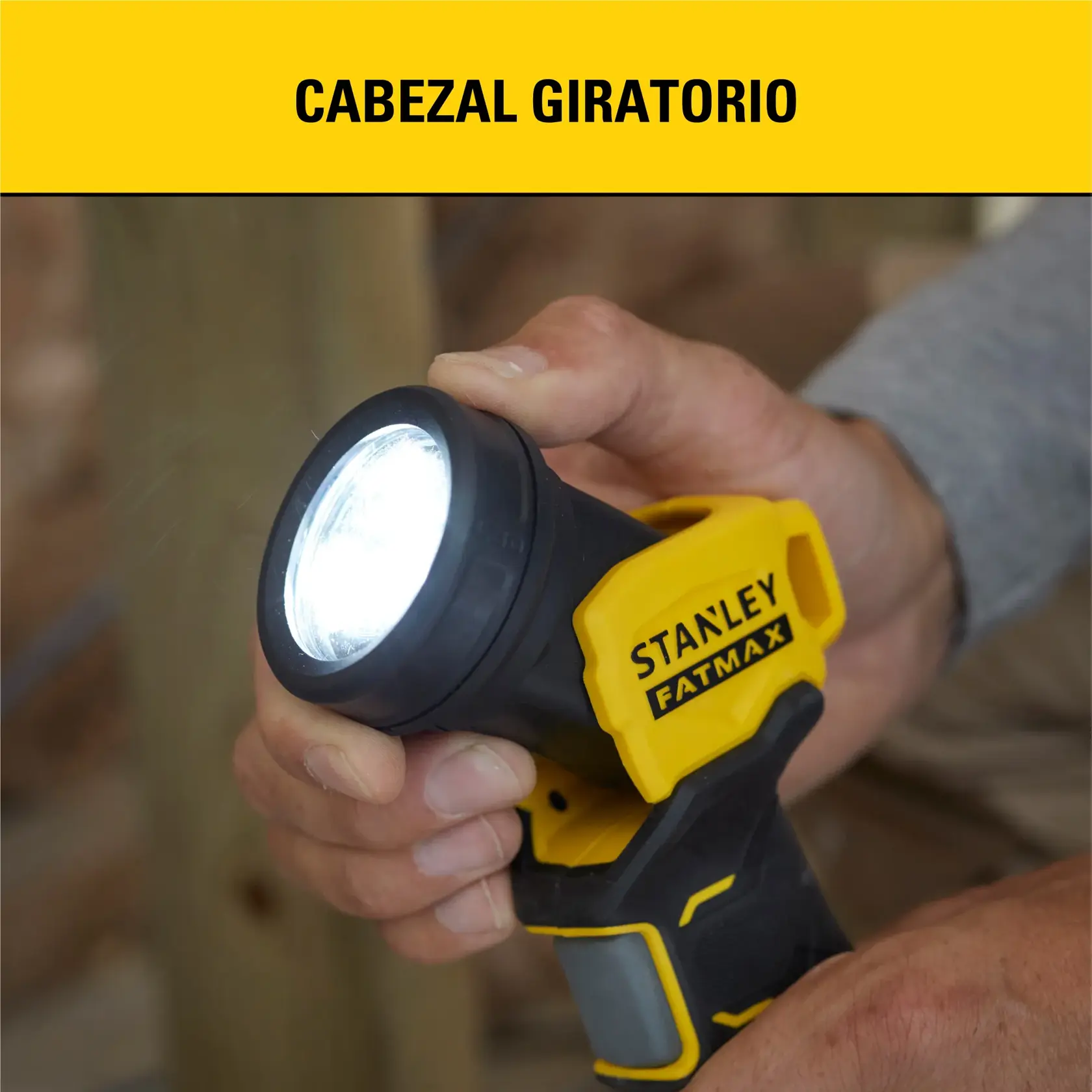 Primer plano de una mano sosteniendo una linterna Stanley Fatmax con cabezal giratorio. La linterna es negra y amarilla, y la luz está encendida. El texto en la parte superior dice 'Cabezal Giratorio'.