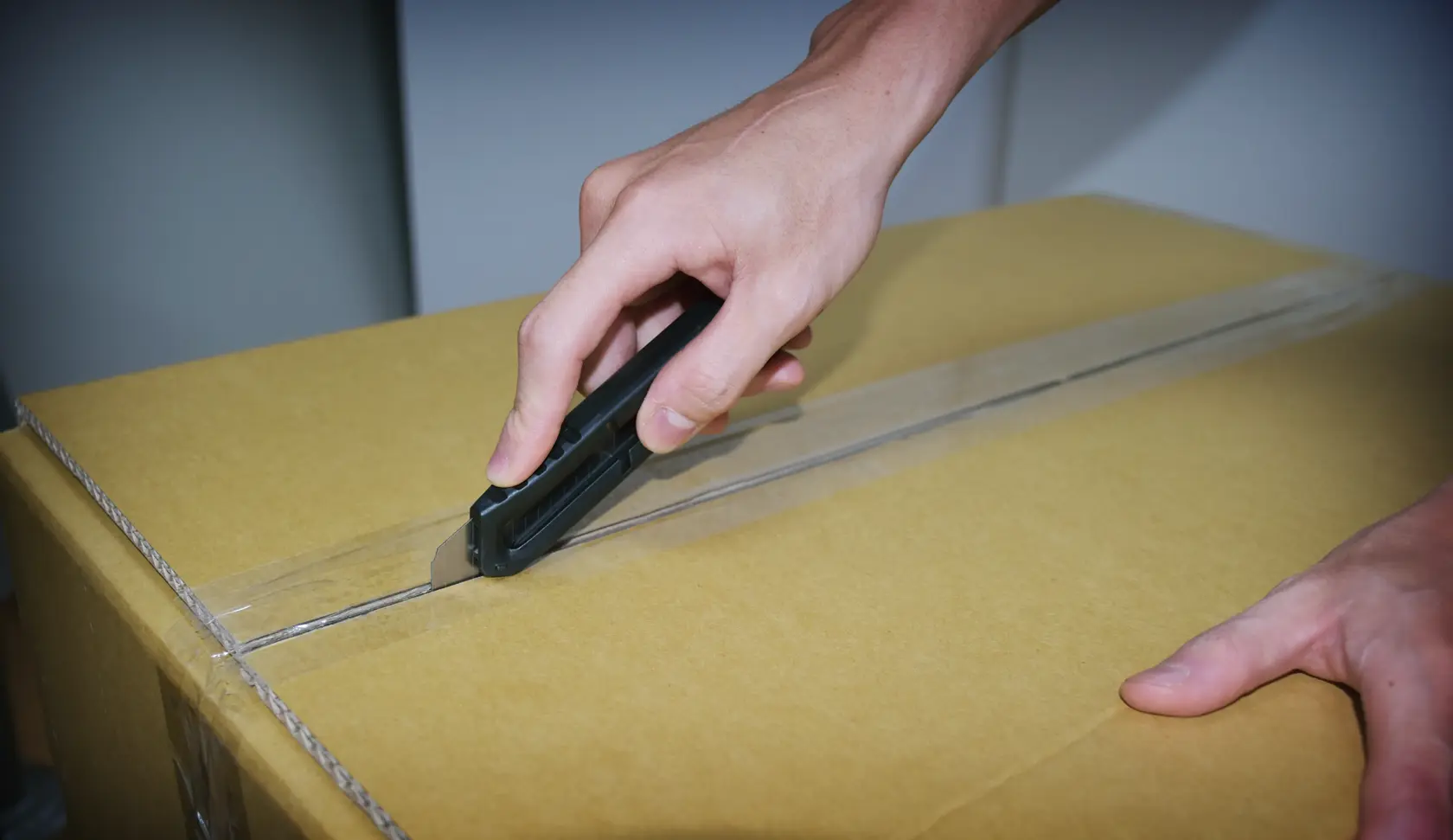 Fotografía del cuchillo STANLEY STHT10323-840 cortando cinta en una caja de cartón, producto en uso, vista cercana.