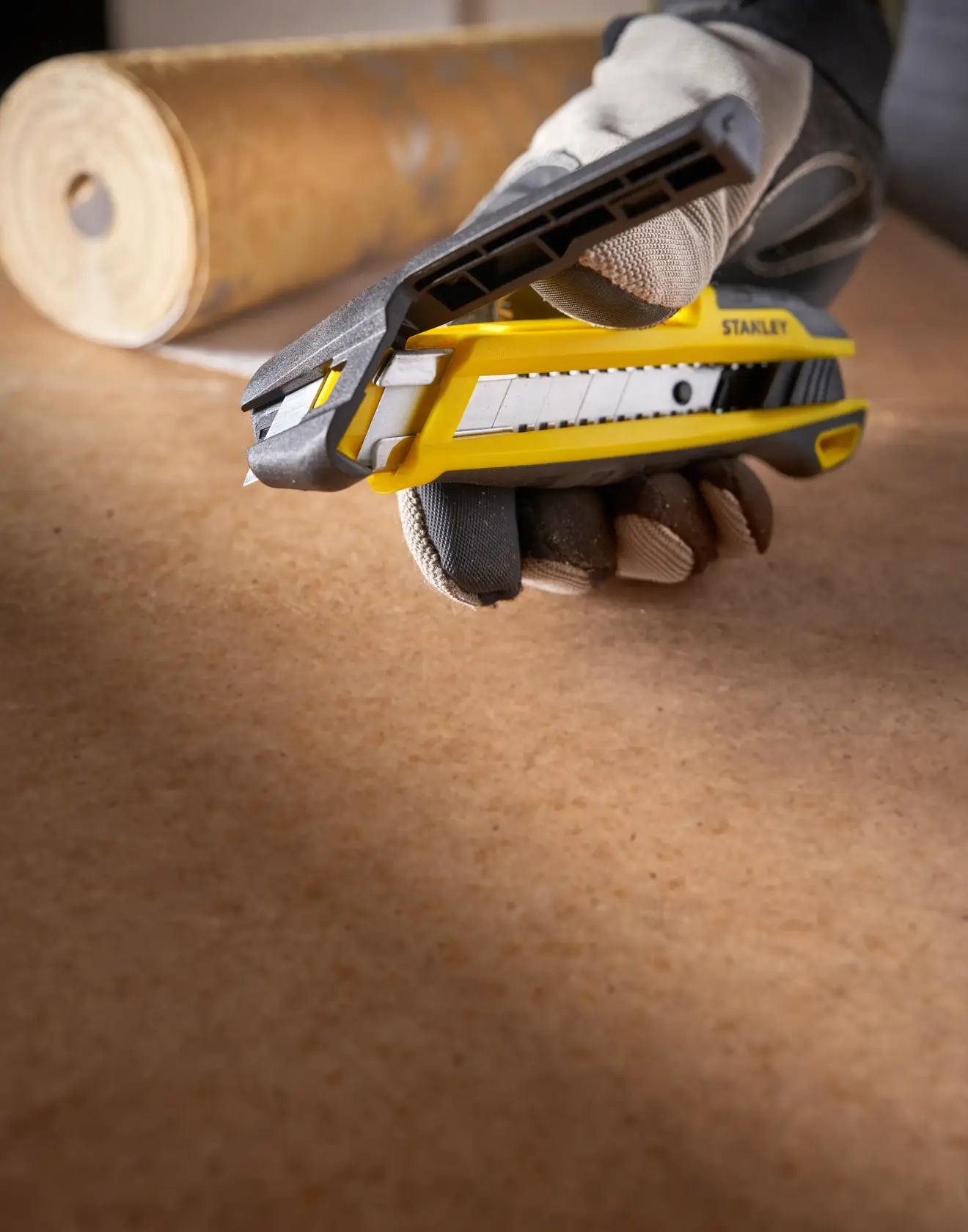 Stanley STHT10501 cuchillo utilitario en mano, amarillo y negro, ángulo lateral, rollo de papel al fondo.