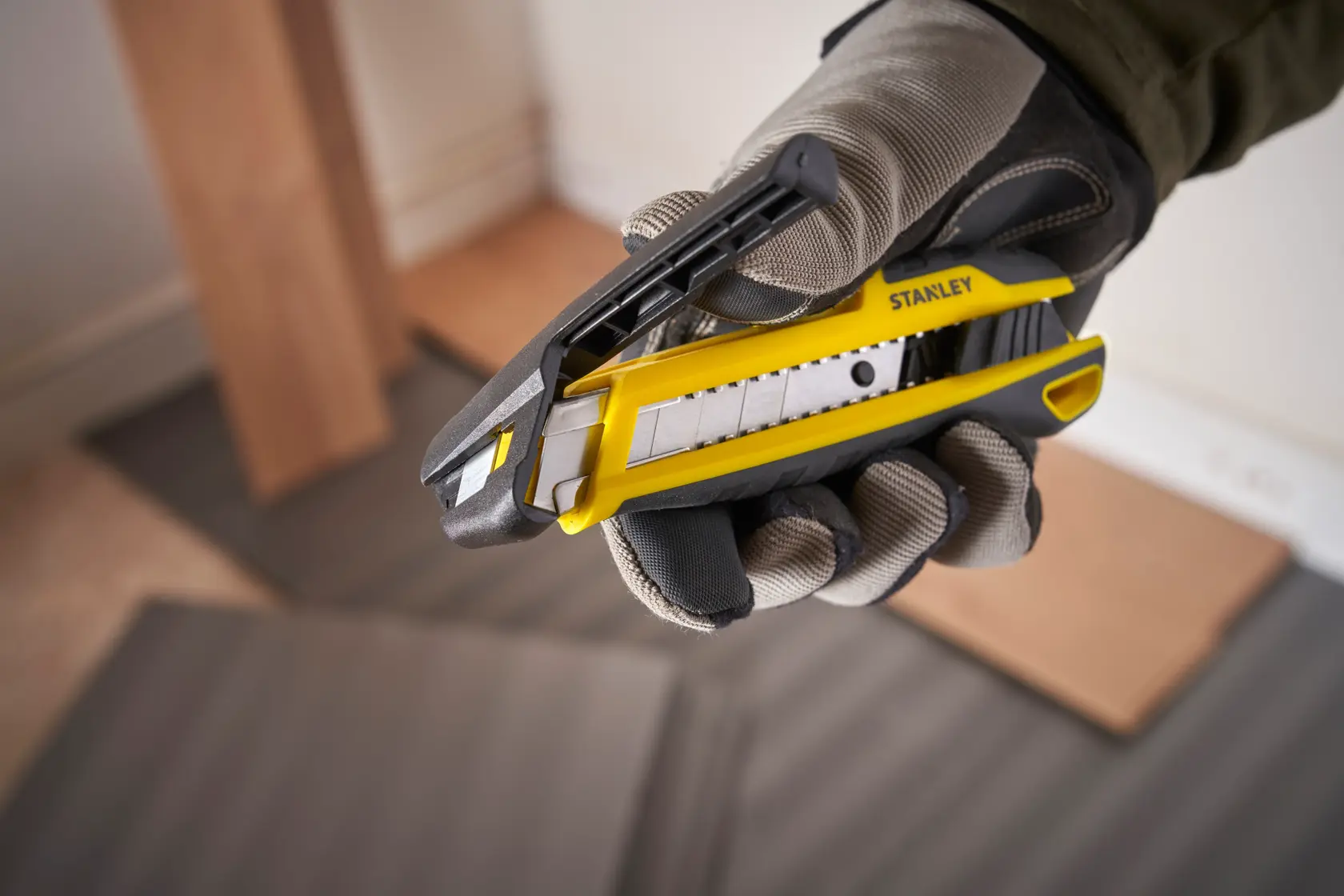 Cuchillo utilitario Stanley STHT10501 con cuerpo amarillo y negro, sostenido por una mano enguantada, vista de cerca.