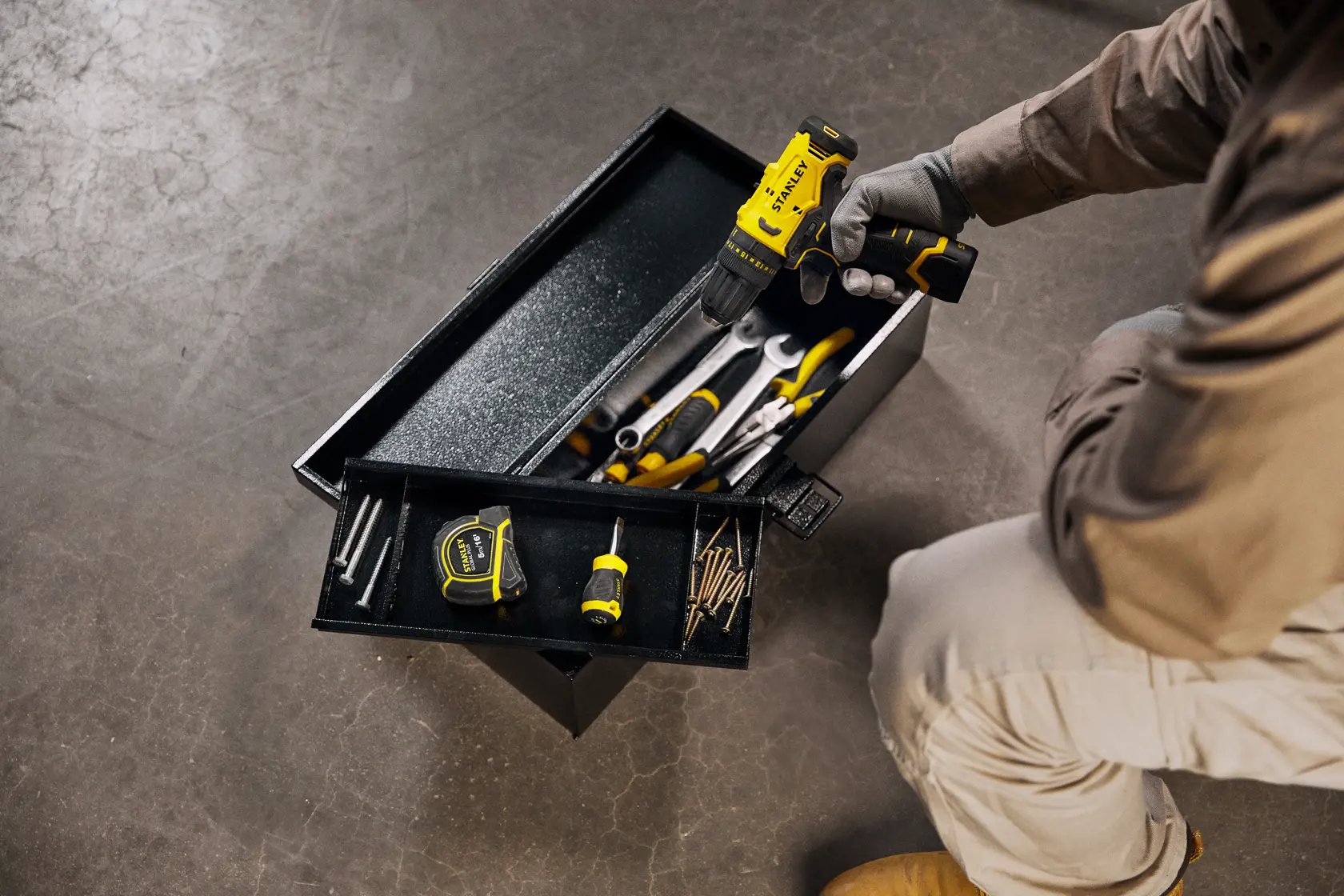 Caja de herramientas STANLEY STST98726LA con cinta métrica, destornillador y taladro, vista superior, en piso de taller.